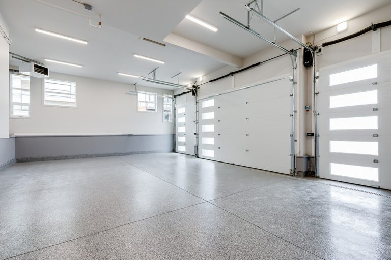 Modern garage interior with white overhead doors, polished concrete floor, and fluorescent ceiling lights