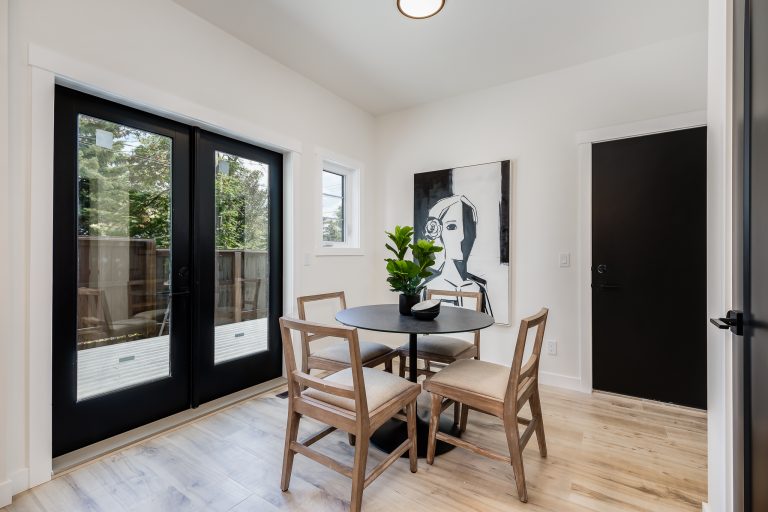 Modern dining area with round table, wooden chairs, black glass doors, and white walls with artwork
